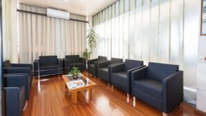 A modern waiting area with dark sofas, a wooden coffee table, and a large window with blinds.