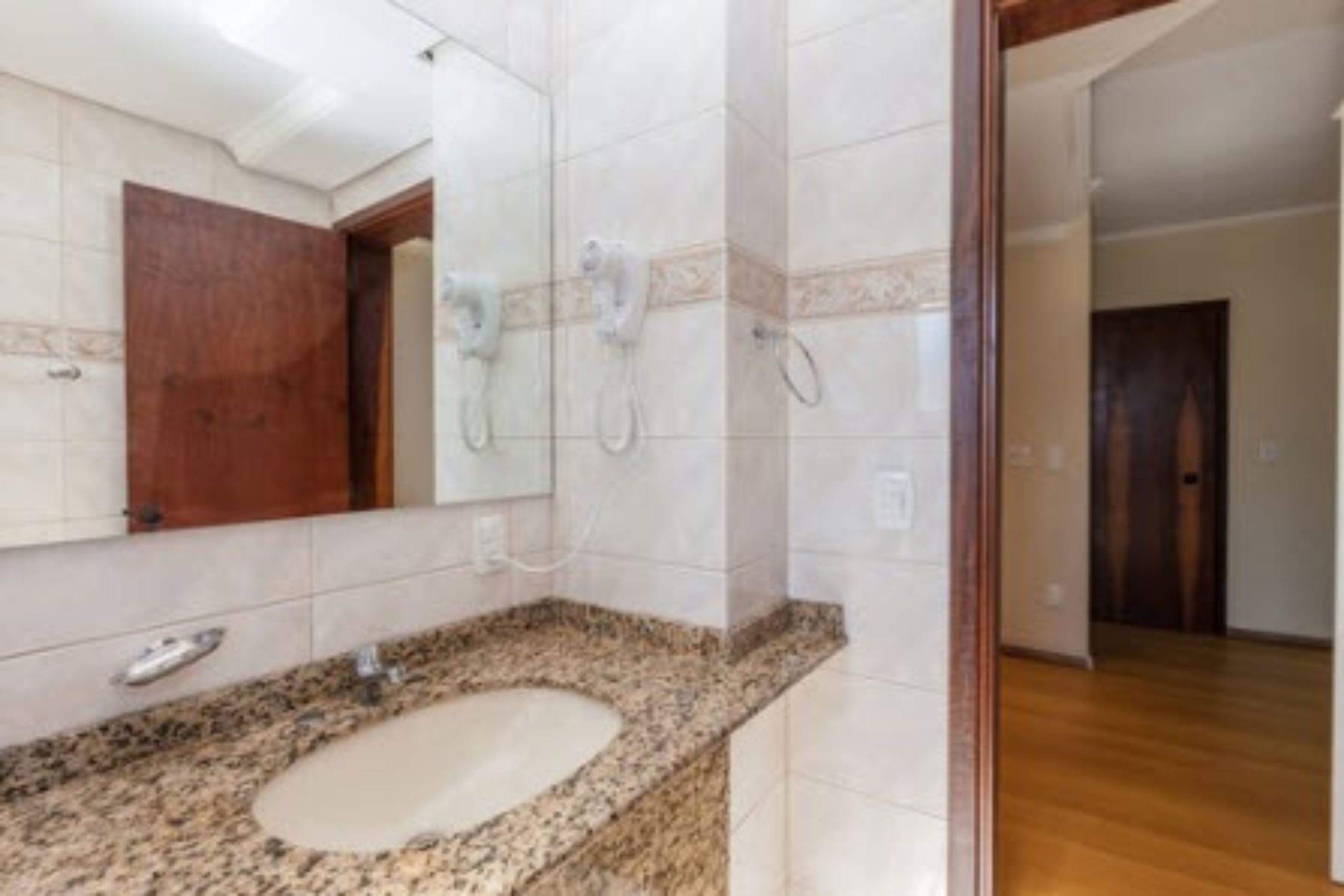 A bathroom with a granite countertop, a sink, a mirror, and a shower with a handheld showerhead.