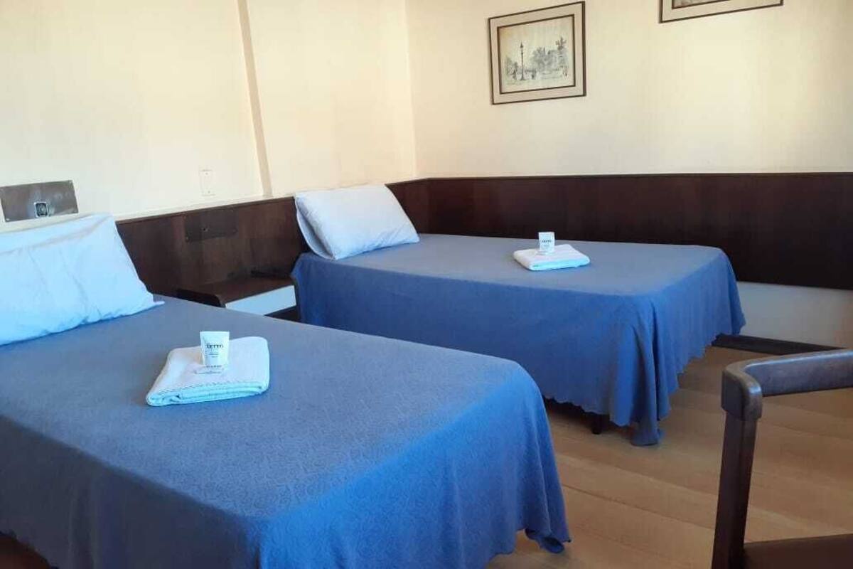 Two single beds with blue linens, a wooden headboard, and a framed picture on the wall.