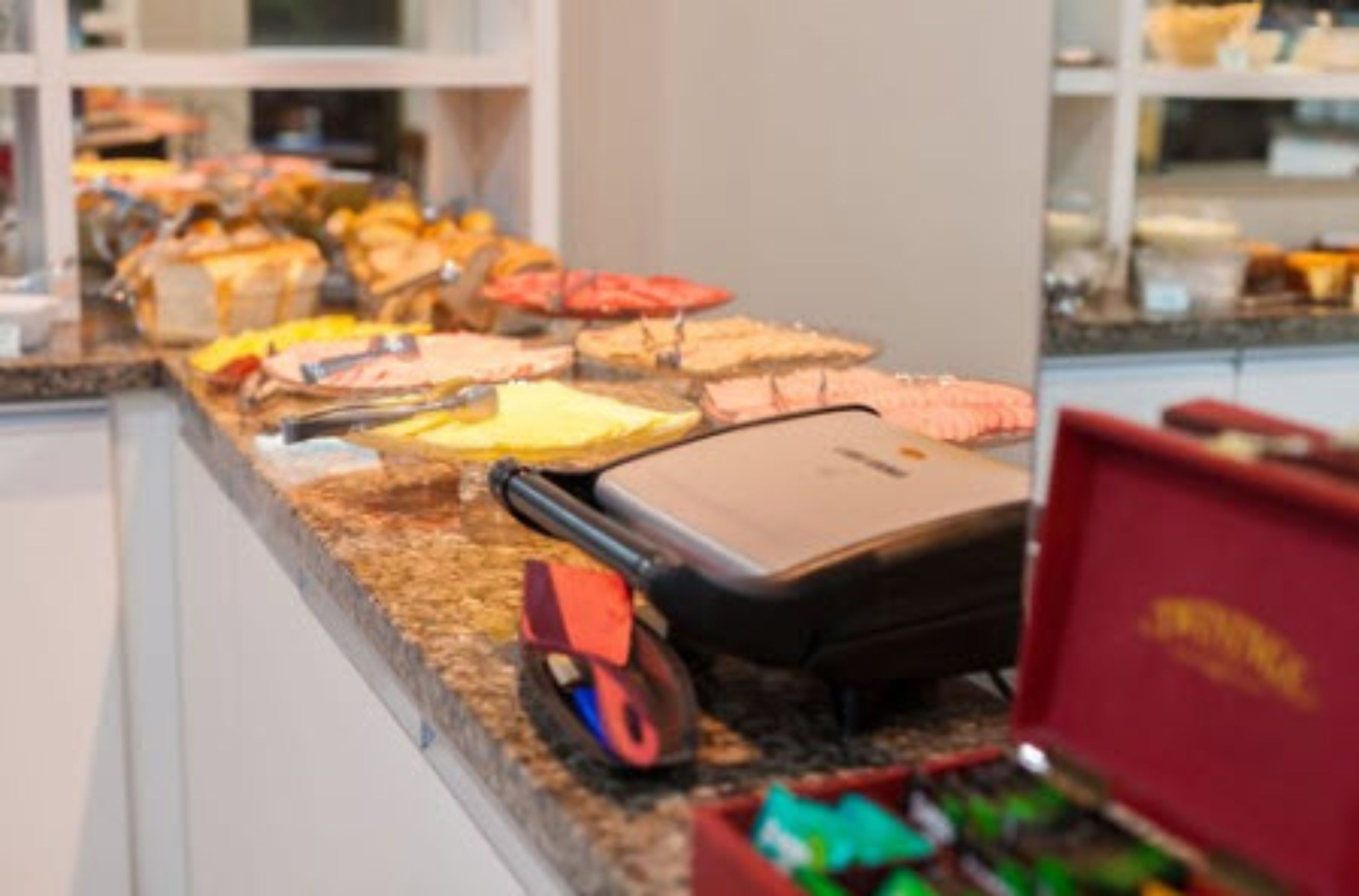 A buffet counter with various food items and a suitcase on the counter.
