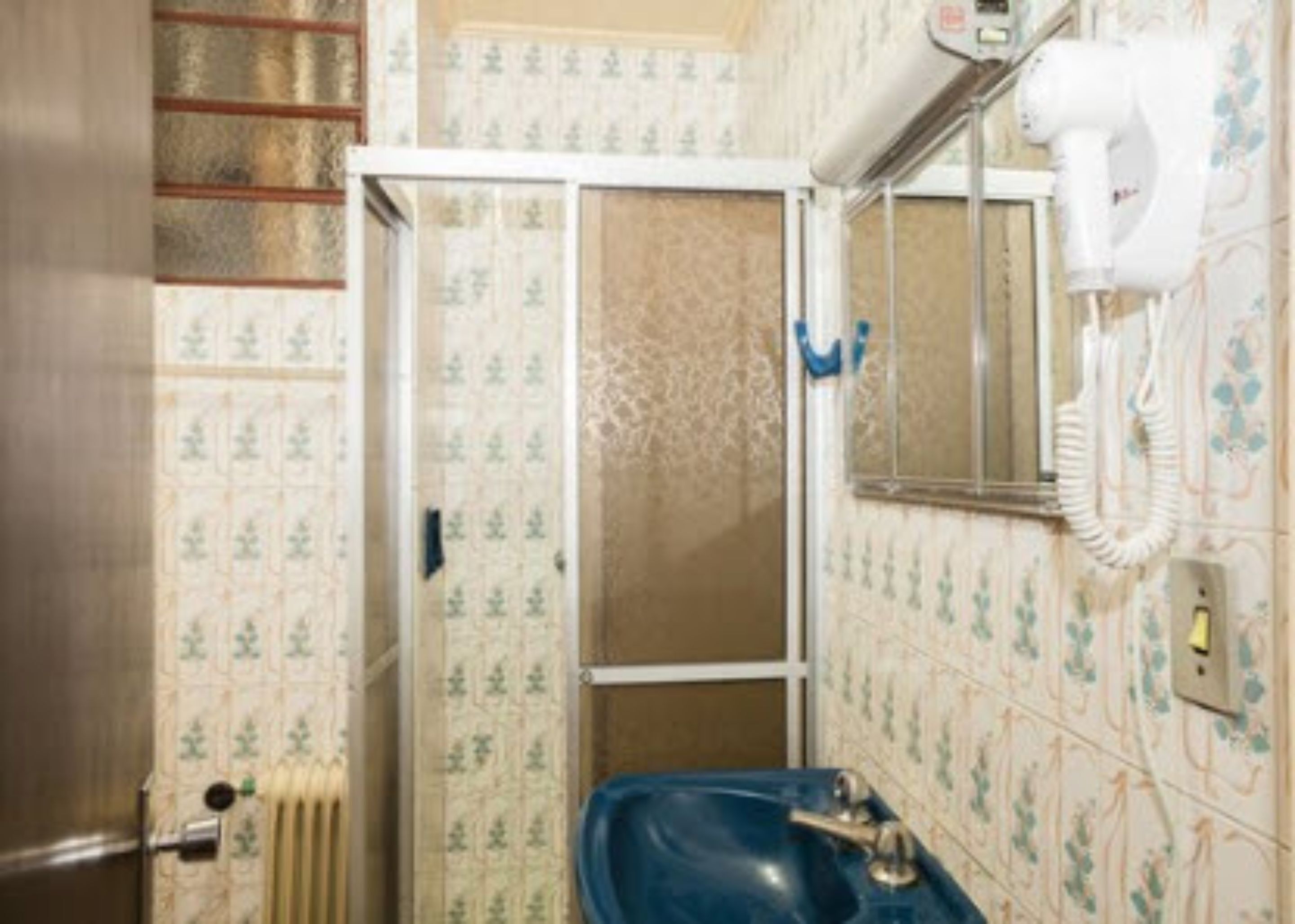 Un baño con un lavamanos azul, un secador blanco y papel tapiz estampado.