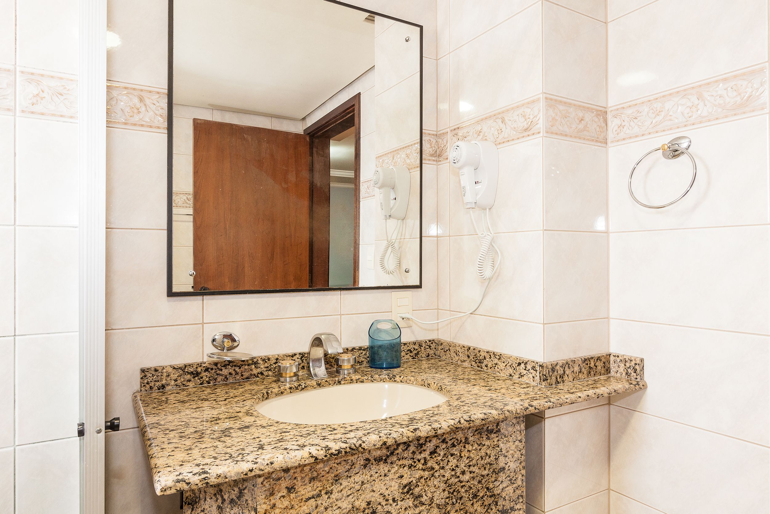 Une salle de bain équipée d’un lavabo avec un plan de travail en granit, d’un miroir, d’un sèche-cheveux et d’un porte-serviettes.