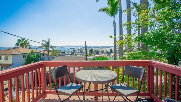 A balcony with two chairs and a table, overlooking a coastal town with palm trees and houses. - 2330/a (San Diego)