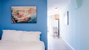 A hotel room with a bed, a painting of boats on the wall, a chair, and a table. - 2330/a (San Diego)