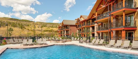 Um hotel com piscina, várias varandas e vista para uma paisagem montanhosa.
