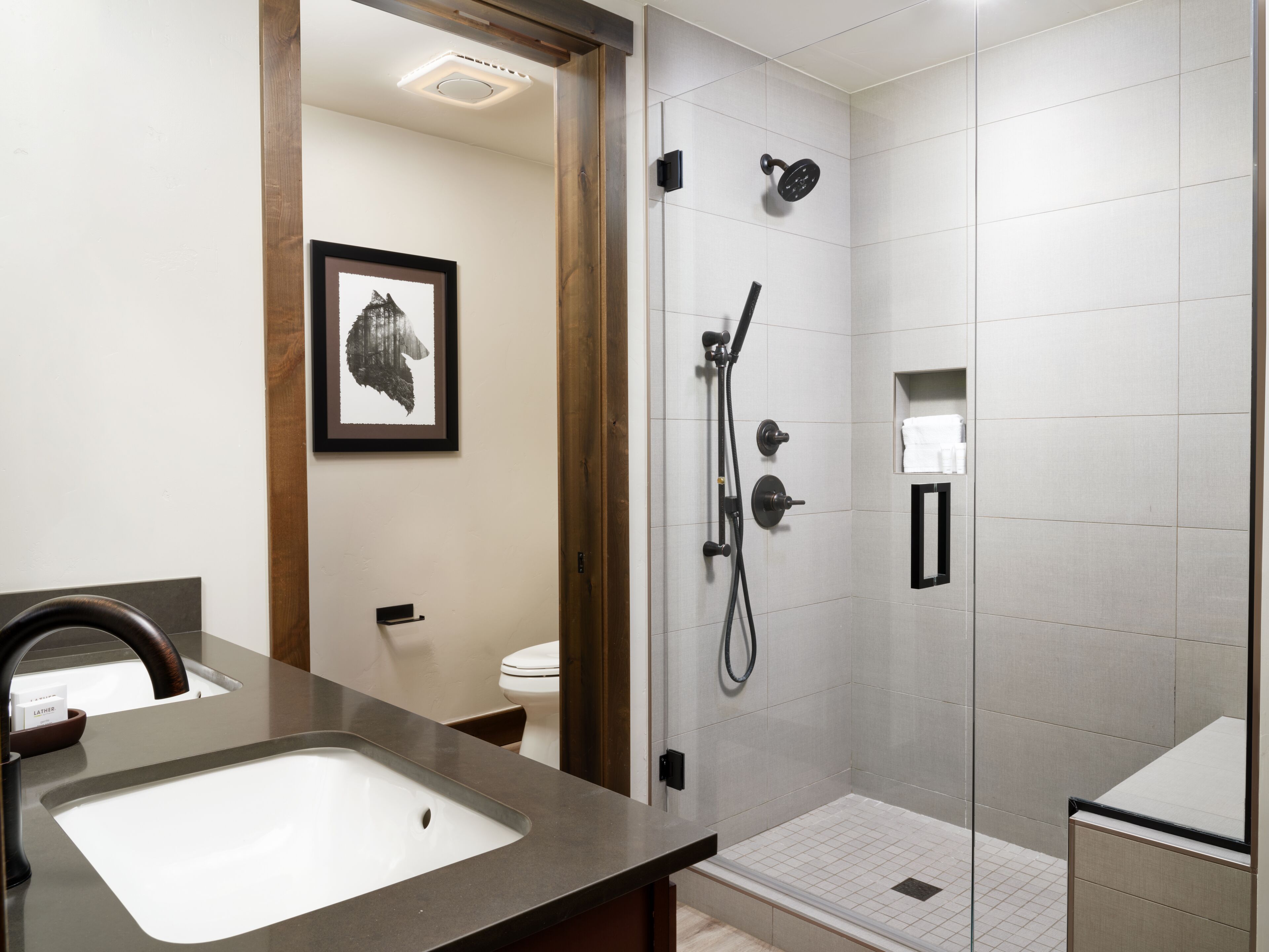 A modern bathroom with a large sink, a shower with a handheld showerhead, and a framed picture on the wall.