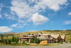 Una cabaña con un letrero de madera llamativo, varias construcciones y un paisaje montañoso de fondo.
