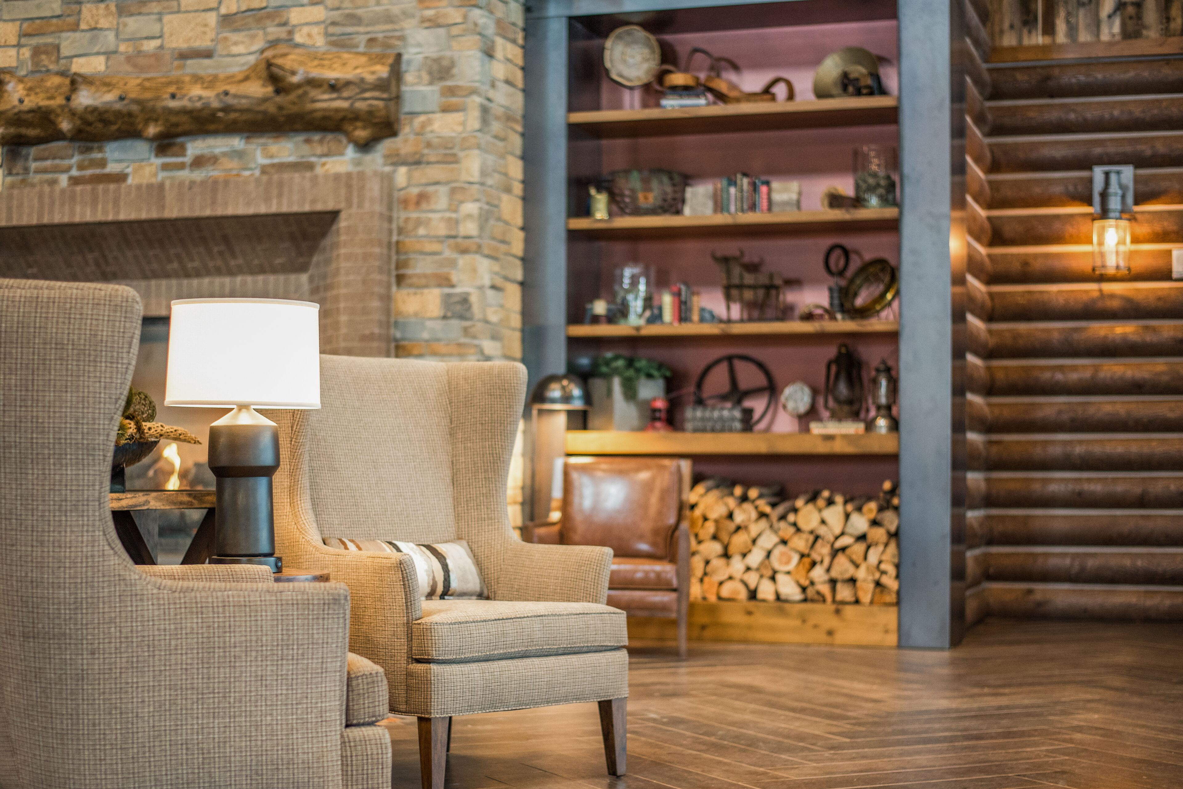 A cozy living room with a fireplace, a comfortable armchair, a wooden bookshelf, and a log storage area.