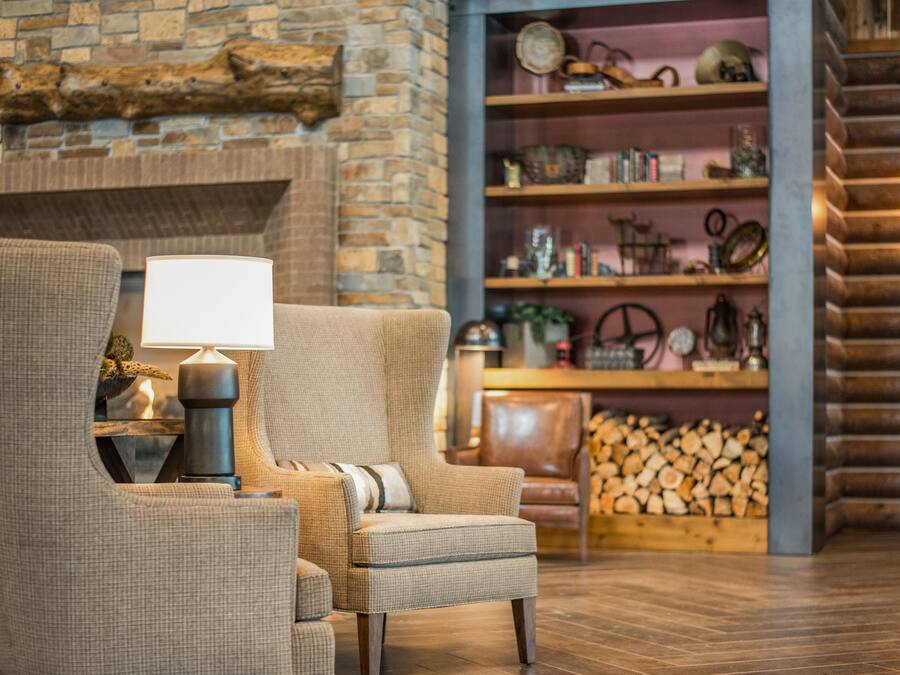A cozy living room with a fireplace, a comfortable armchair, a wooden bookshelf, and a log storage area.