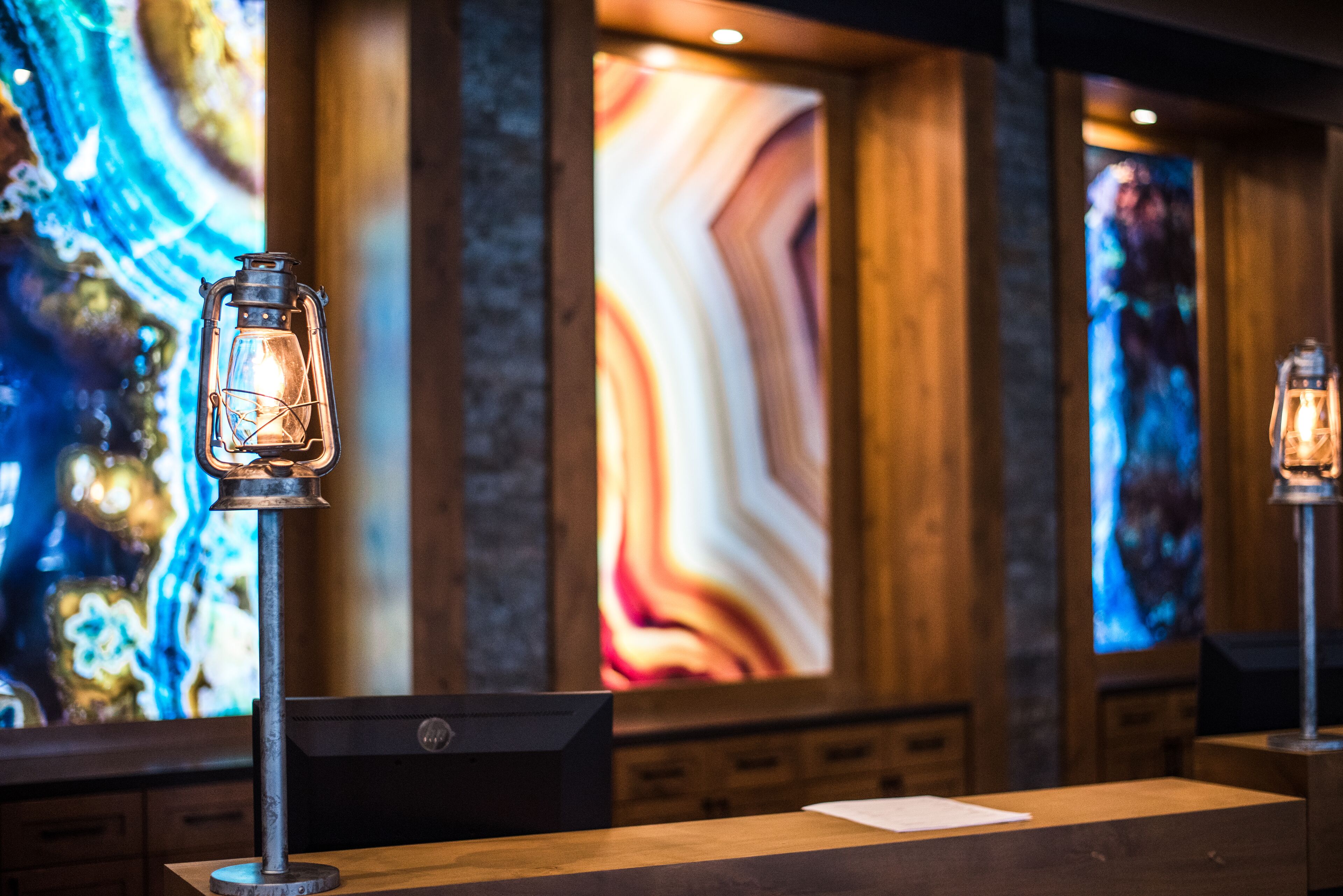 A wooden reception desk with two vintage-style lanterns, a large abstract painting on the wall, and a modern desk lamp.