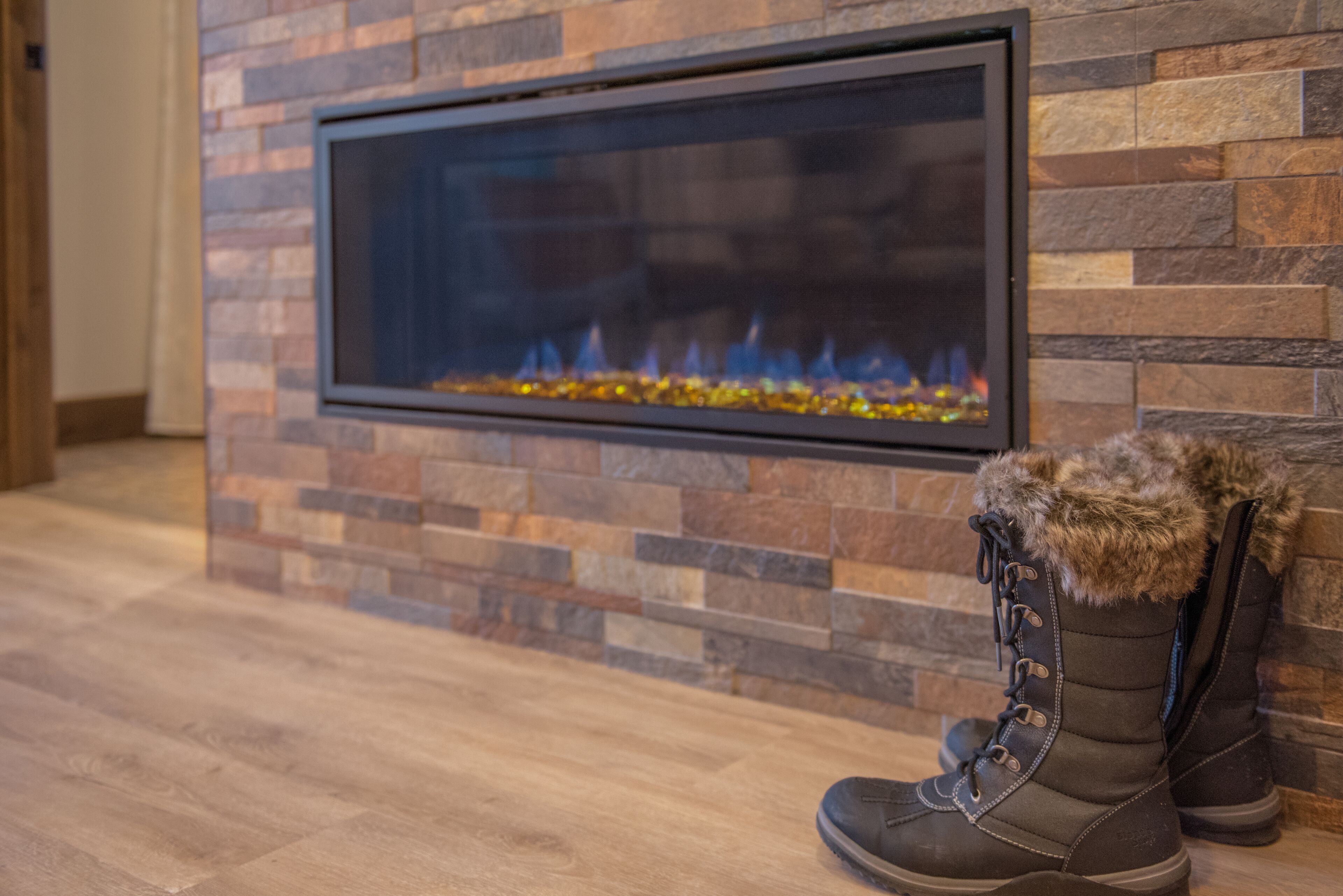 A fireplace with a stone wall, a pair of boots with fur trim, and a wooden floor.