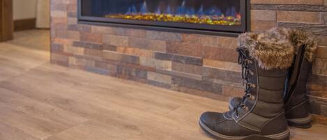A fireplace with a stone wall, a pair of boots with fur trim, and a wooden floor.