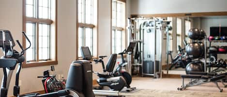 A gym with exercise equipment, large windows, and a mirror.