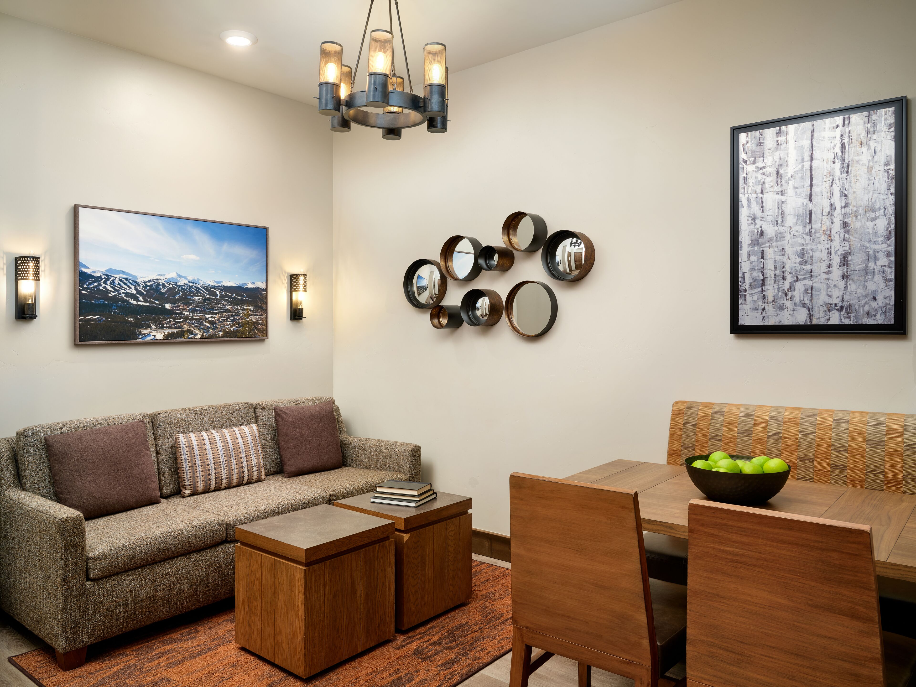 A modern living room with a sofa, coffee table, dining table, chairs, and a chandelier.