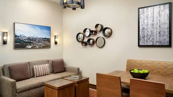 A modern living room with a sofa, coffee table, dining table, chairs, and a chandelier.