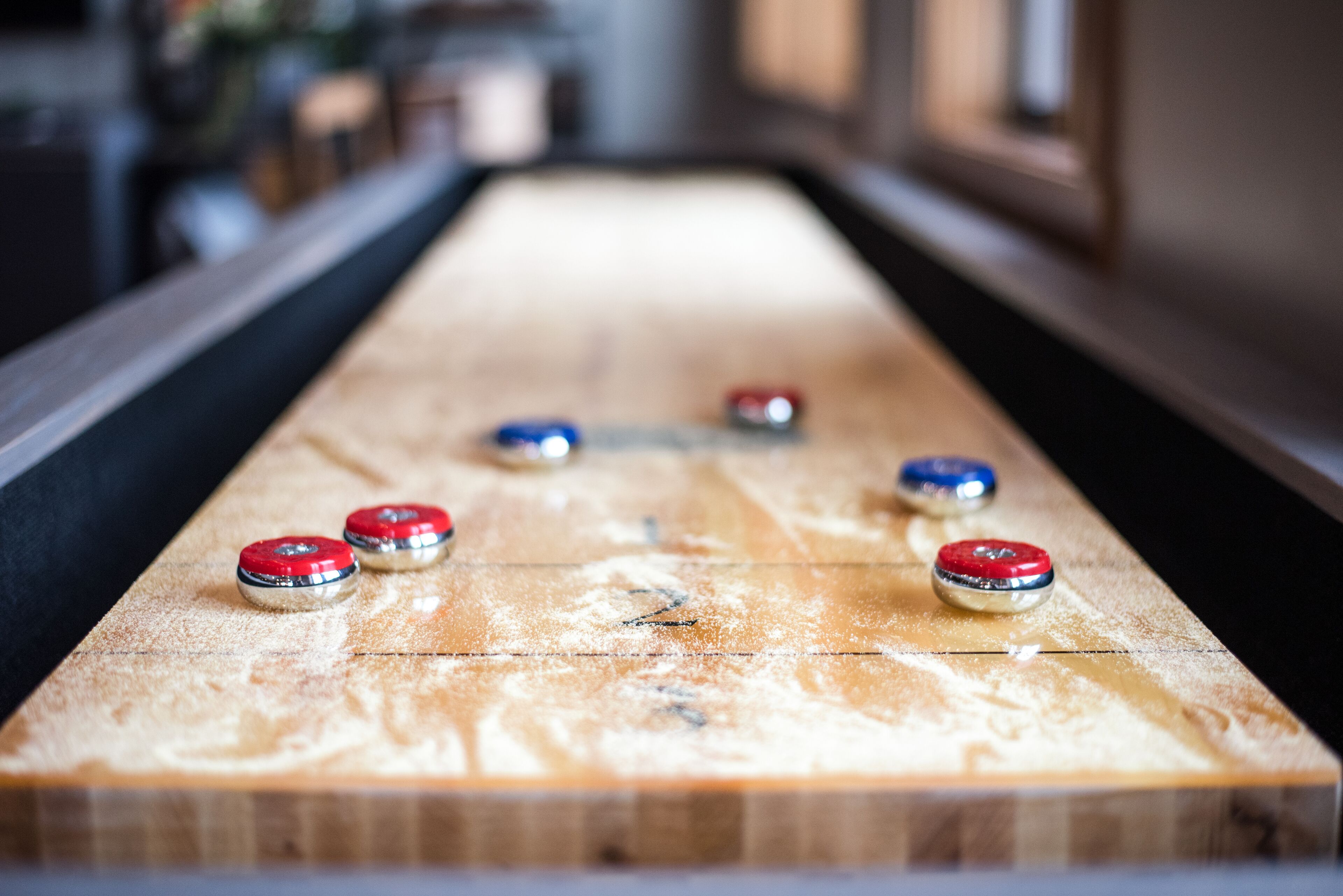 A shuffleboard table with six pucks in red, blue, and silver colors.