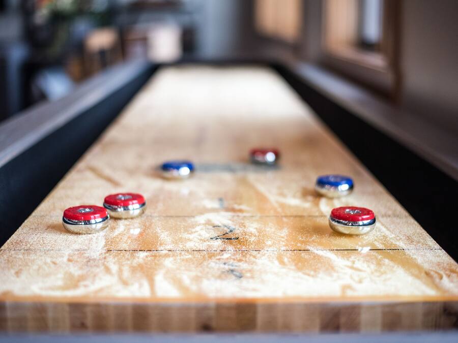 A shuffleboard table with six pucks in red, blue, and silver colors.