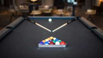 A pool table with a set of colorful balls in the center, surrounded by chairs and tables in a dimly lit room.