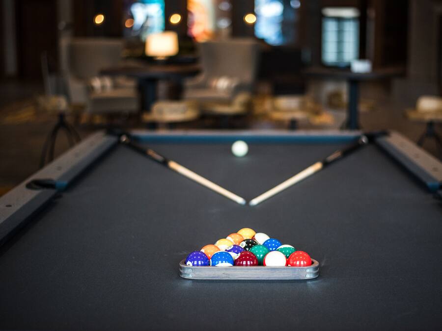 A pool table with a set of colorful balls in the center, surrounded by chairs and tables in a dimly lit room.