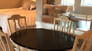 A dining area with a round table and white chairs, a bed with a headboard in the background, and artwork on the walls. - Perfect Getaway overlooking the Puget Sound, Close to Ruston Point and UPS (Tacoma)