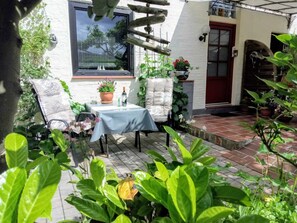 A patio with a table and chairs, potted plants, and a window overlooking a garden.