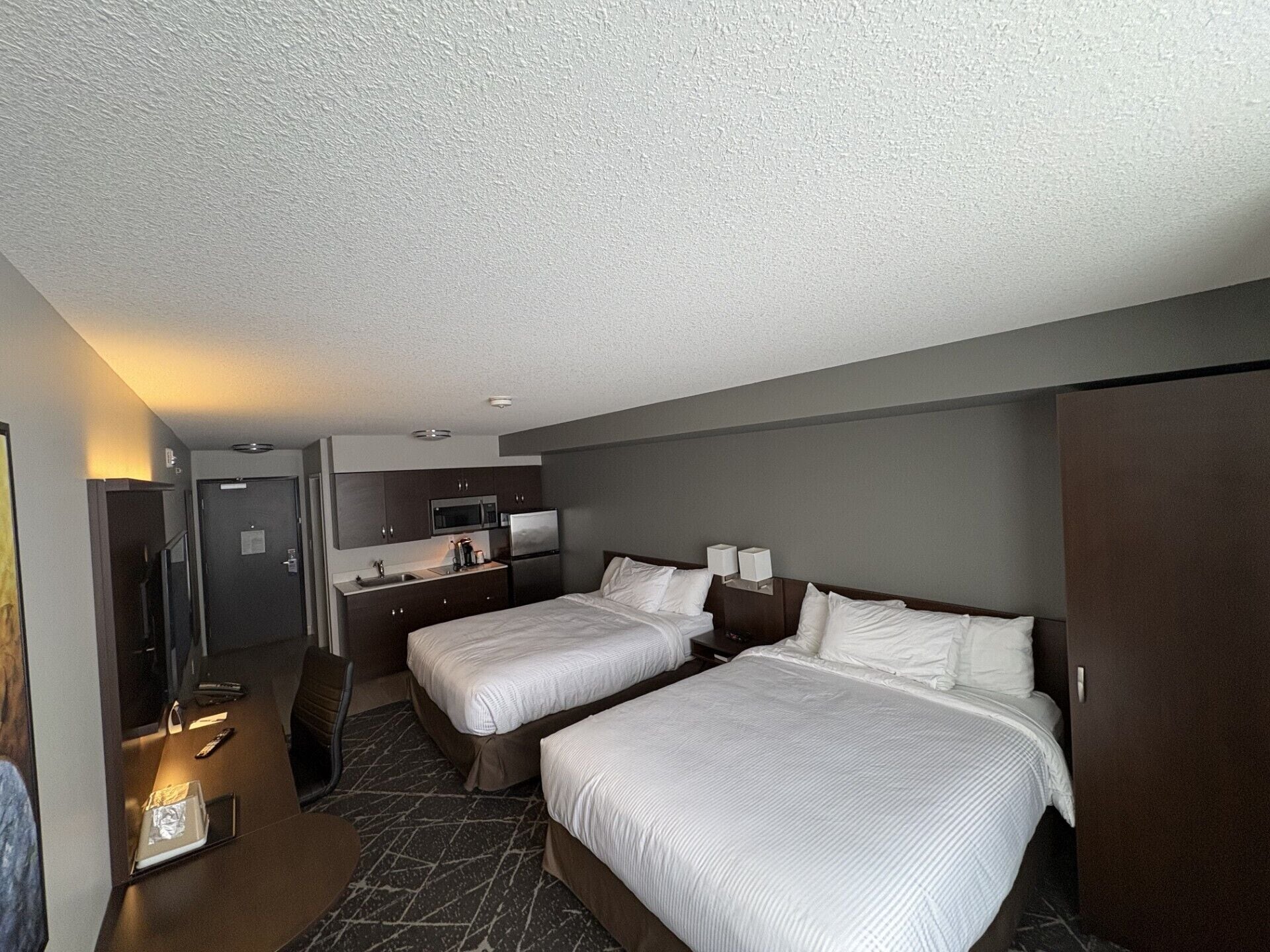 Une chambre d’hôtel avec deux lits, une kitchenette, un bureau et une armoire.