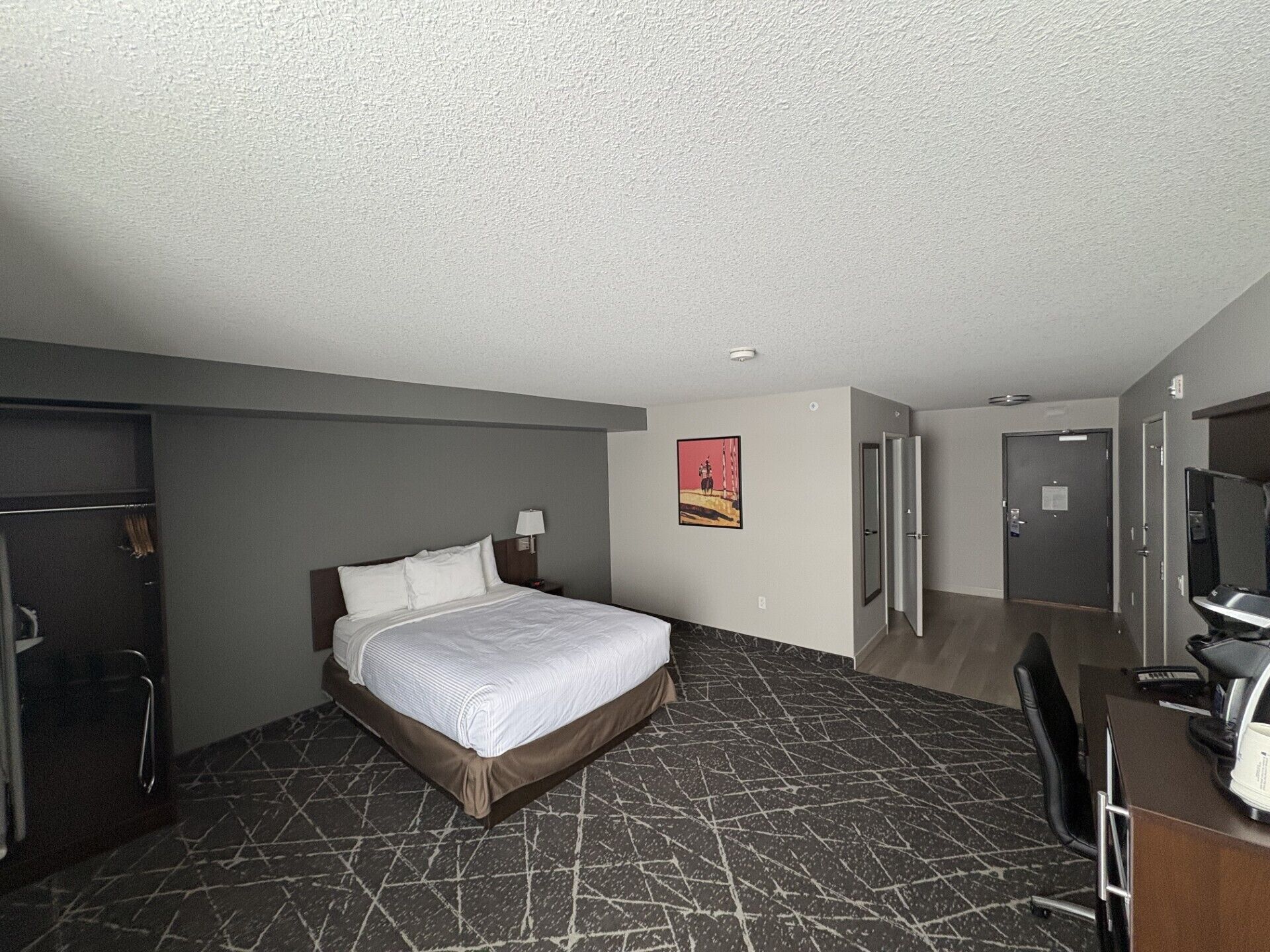 A hotel room with a bed, a desk, a chair, a wardrobe, and a door.