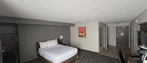A hotel room with a bed, a desk, a chair, a wardrobe, and a door.