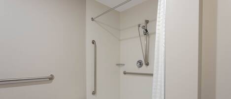 A modern bathroom with a walk-in shower, grab bars, and a small white bench.