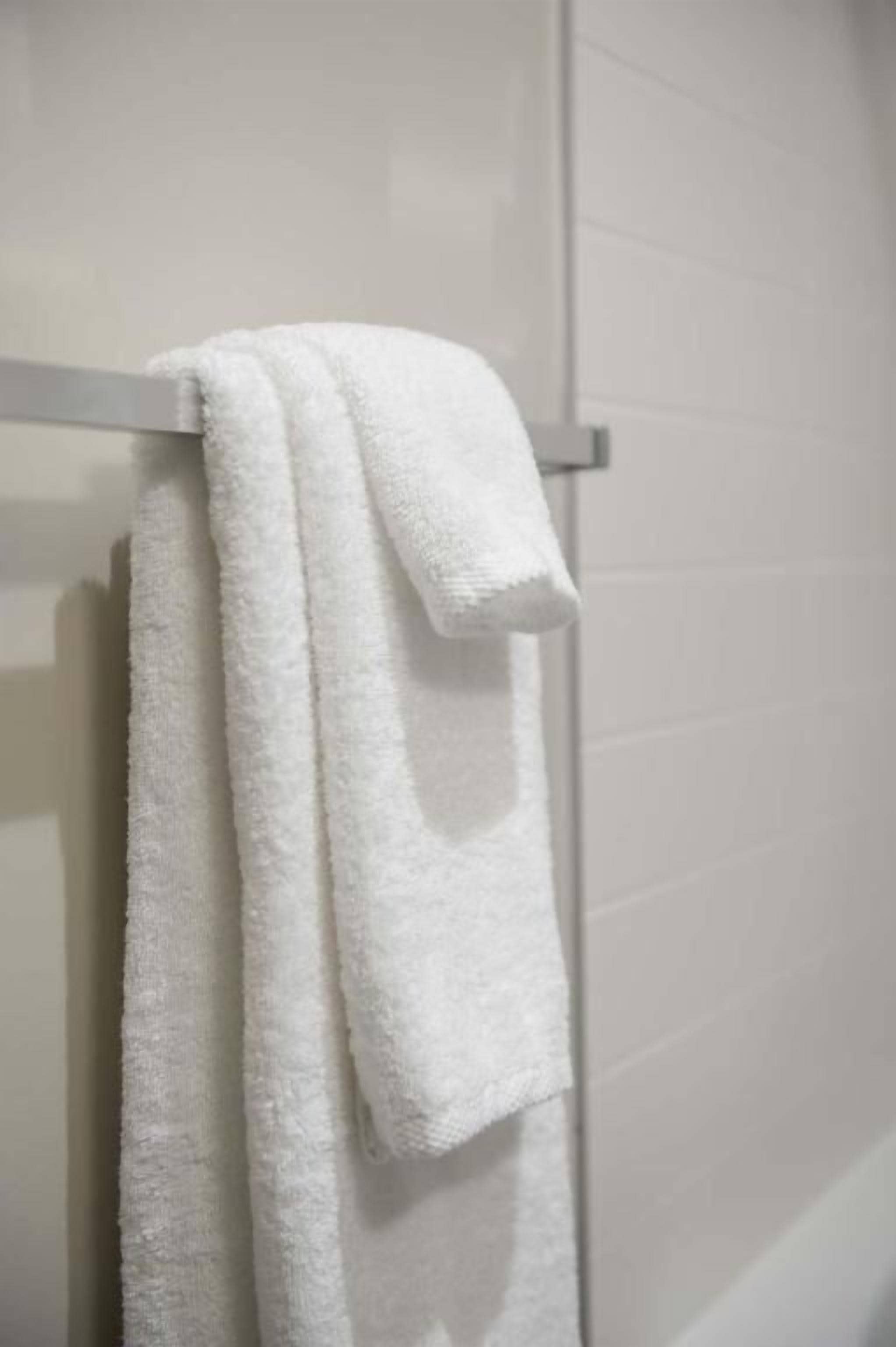 A white towel hanging on a metal towel rack in a bathroom with white tiled walls.