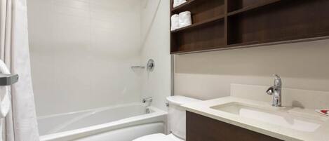 Un baño moderno con bañera, inodoro y tocador con estantes.