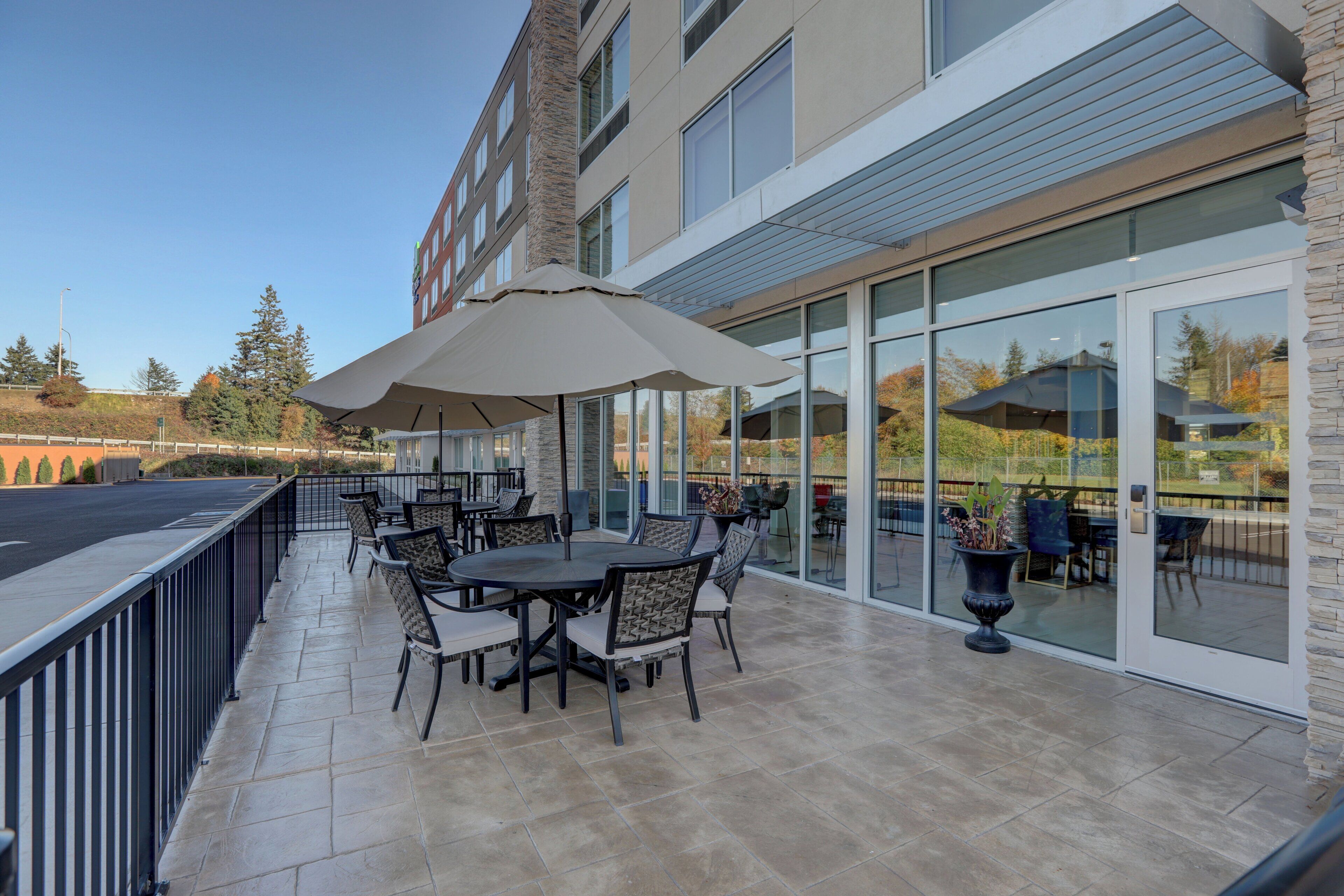 An outdoor patio with tables and chairs, a large umbrella, and a glass door leading to an interior space.