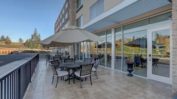 An outdoor patio with tables and chairs, a large umbrella, and a glass door leading to an interior space.