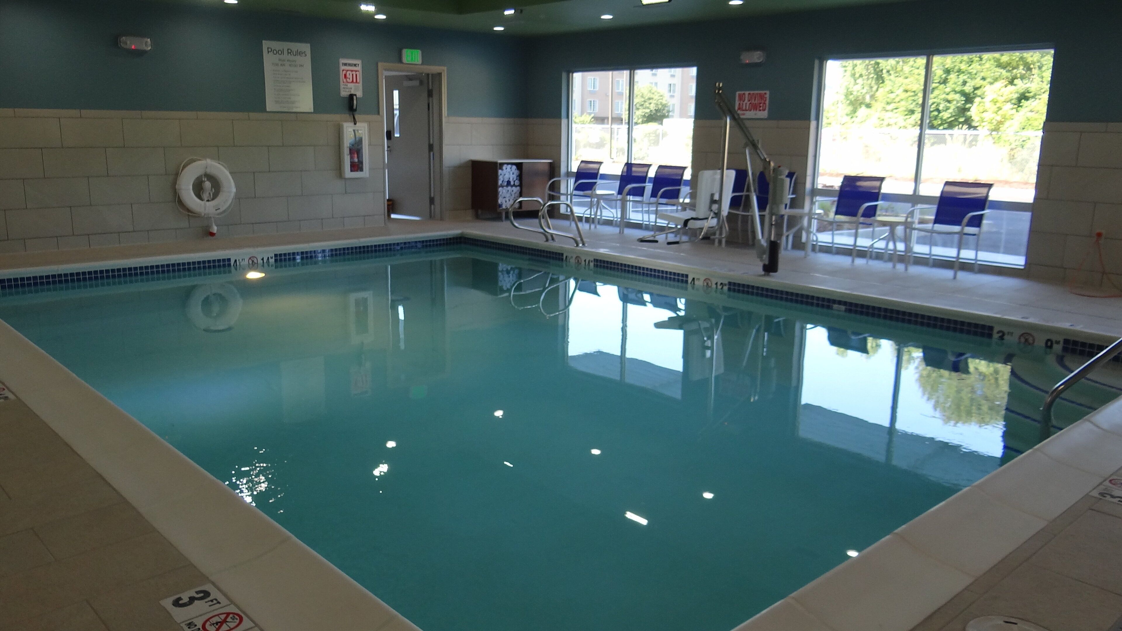 Une piscine intérieure à l’eau claire, avec un poste de surveillance pour le sauveteur et un panneau indiquant les règles à respecter.