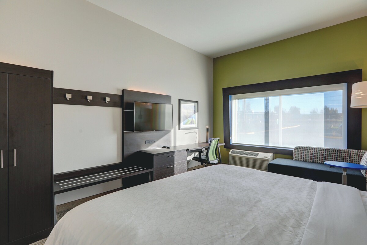A hotel room with a bed, a desk, a chair, a TV, a window, and a wardrobe.