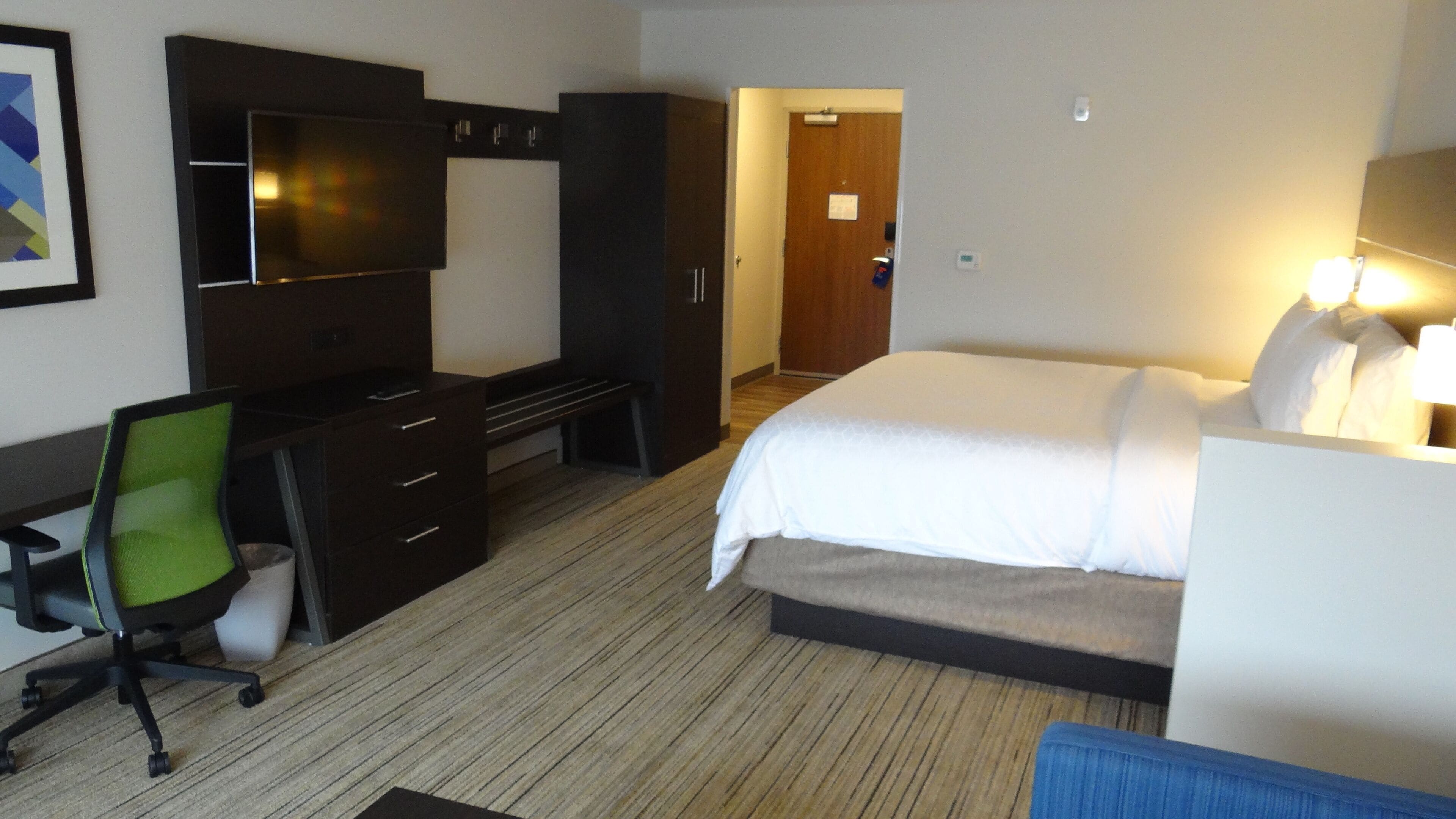 A hotel room with a bed, a desk with a chair, a television, and a wardrobe.