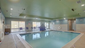 A swimming pool with a tiled deck, a covered seating area with chairs, and a door leading to a shower area. - Holiday Inn Express & Suites Auburn Downtown by IHG (Auburn)