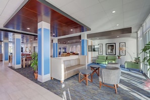 A modern lobby with a reception desk, seating area, and a large window providing natural light. - Holiday Inn Express & Suites Auburn Downtown by IHG (Auburn)