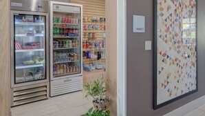 A clean, modern interior with a vending machine, a refrigerated display, and a wall-mounted sign indicating a market area. - Holiday Inn Express & Suites Auburn Downtown by IHG (Auburn)