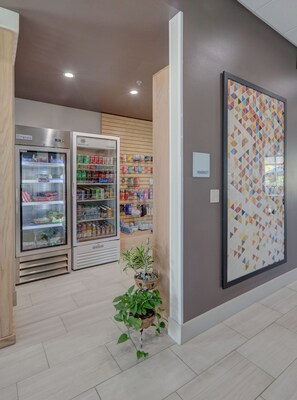 A clean, modern interior with a vending machine, a refrigerated display, and a wall-mounted sign indicating a market area. - Holiday Inn Express & Suites Auburn Downtown by IHG (Auburn)