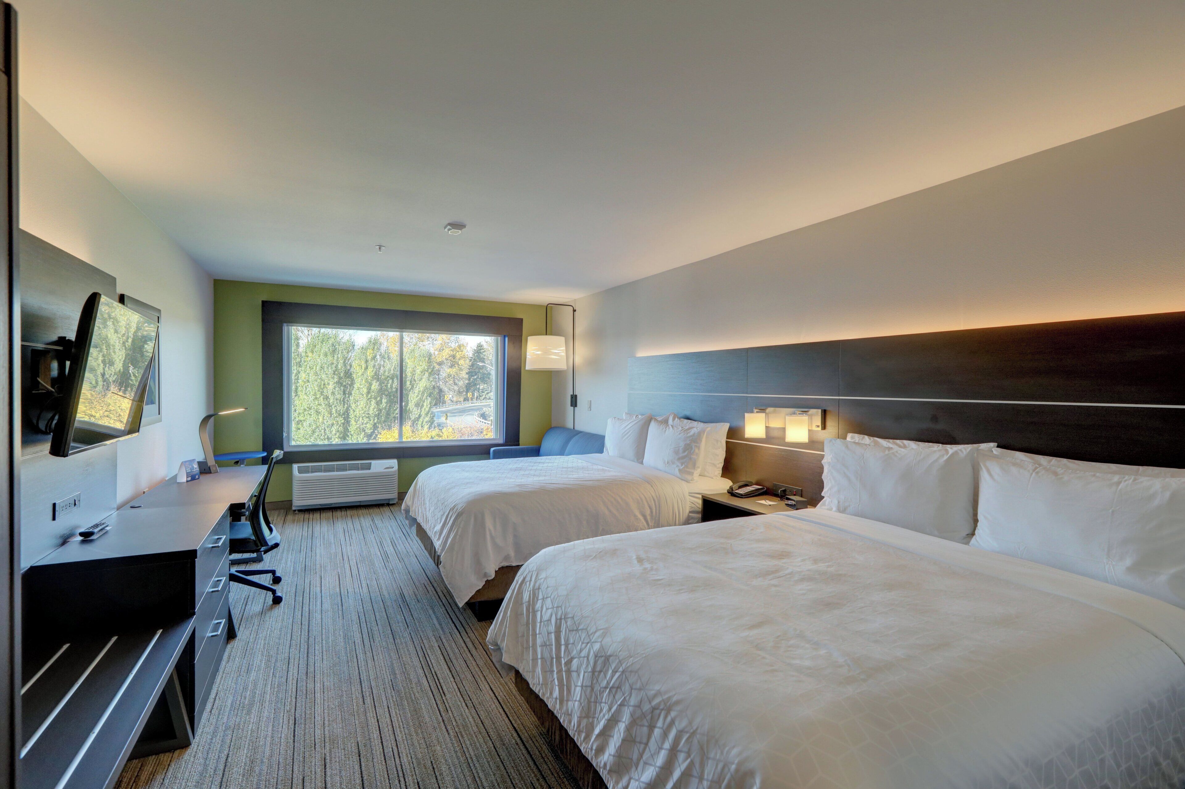 A hotel room with two beds, a desk, a TV, and a large window.
