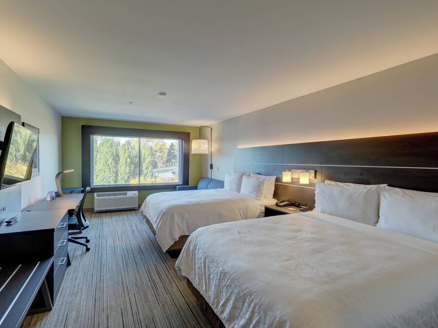 A hotel room with two beds, a desk, a TV, and a large window.