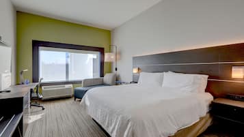 A hotel room with a large bed, a desk with a chair, a window with a view, and a bedside table with a lamp.
