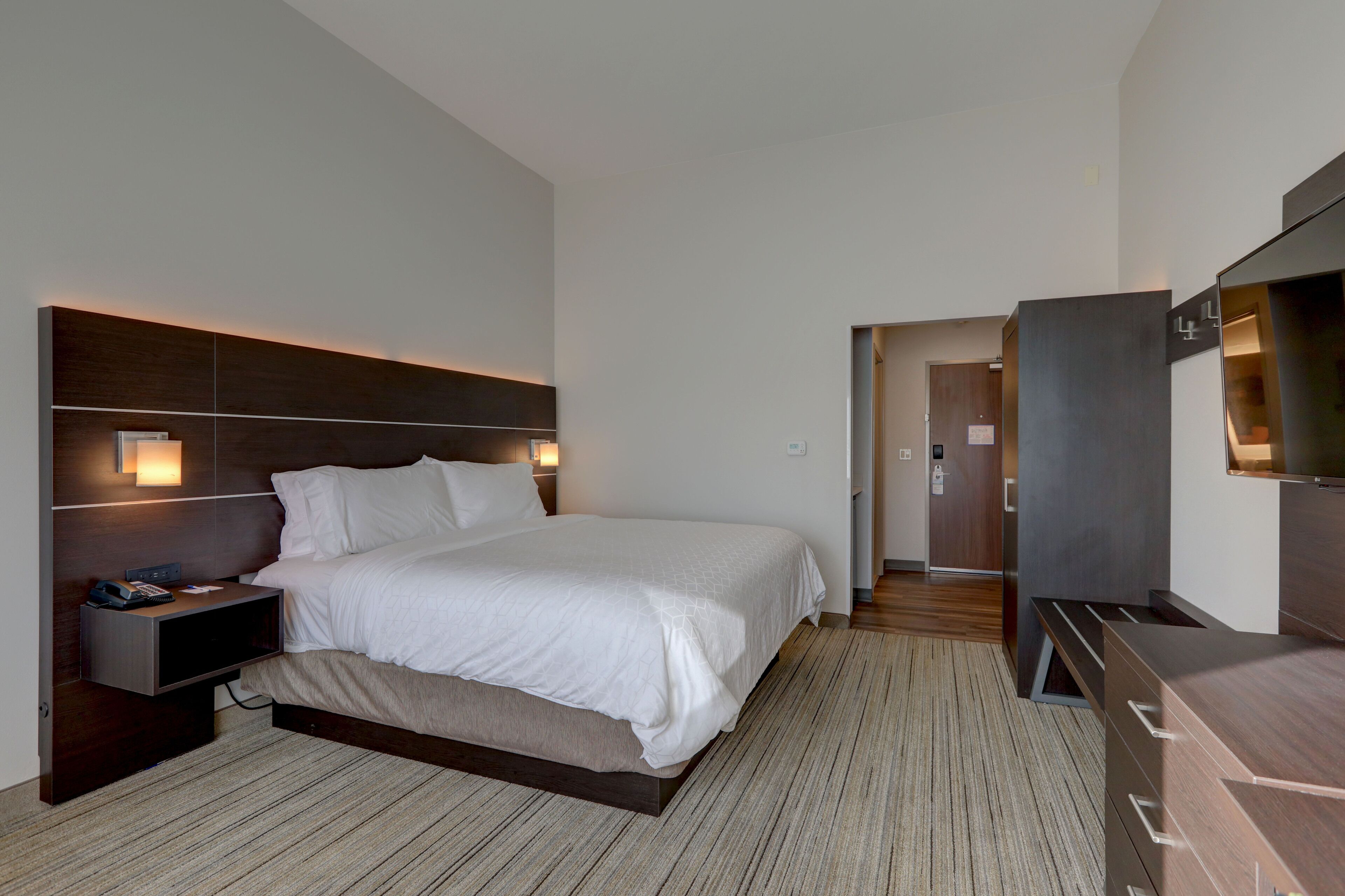 A modern hotel room with a large bed, bedside tables, a flat-screen TV, and a walk-in closet.