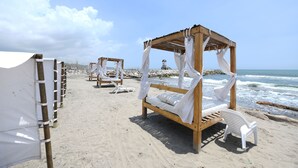 A beach with wooden canopy beds and white chairs. - Imagine Beach (Puerto Colombia)