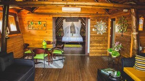 A cozy log cabin interior with a dining area, a bed with a canopy, and a living room with a sofa and a coffee table. - Imagine Beach (Puerto Colombia)