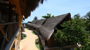 A row of thatched-roof bungalows with a clear view of the sea, a paved walkway, and lush greenery. - Imagine Beach (Puerto Colombia)