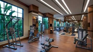 A spacious gym with various exercise equipment, large windows, and a wooden floor.