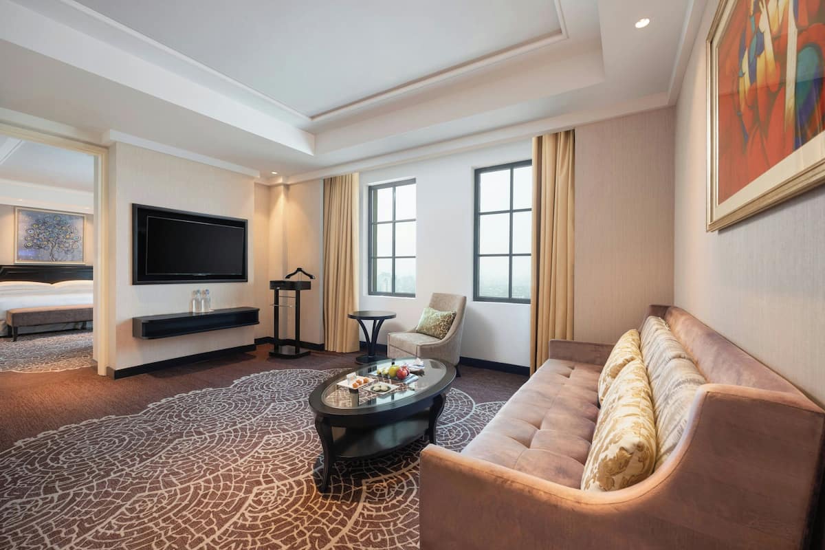 Ein Hotelzimmer mit einem großen Bett, einer Couch, einem Couchtisch, einem Fernseher und einem Gemälde an der Wand.