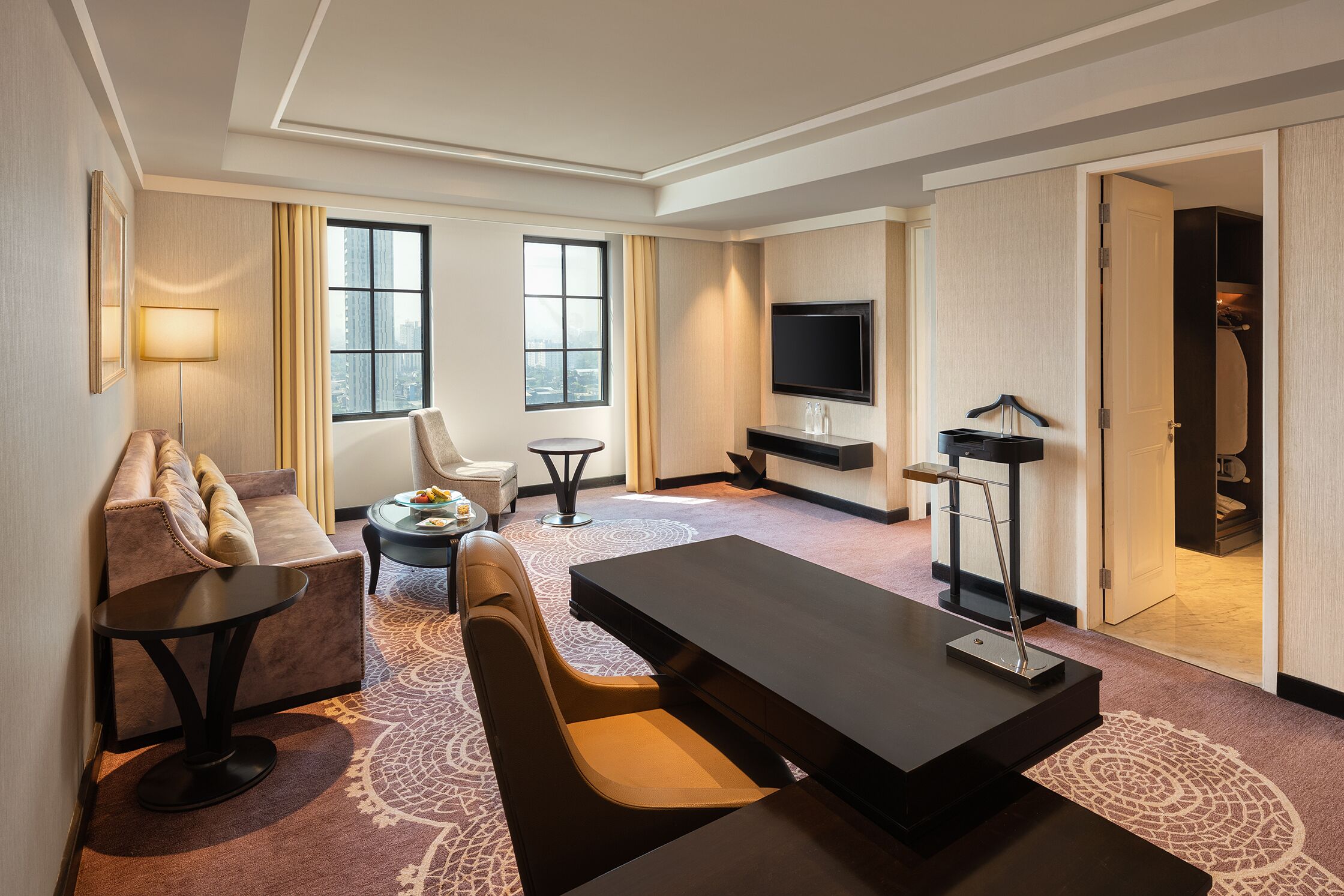 Habitación de hotel con sofá, una mesa de comedor, televisor y vista a la ciudad a través de amplias ventanas.